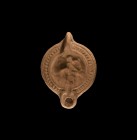 Roman Oil Lamp with Horseman
2nd-3rd century AD. A ceramic oil lamp with short round nozzle, pierced lug handle to the rear, geometric border around ...