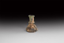 Roman Glass Dropper Flask
3rd century AD. An iridescent glass with conical body and concave underside, applied trail collar, tapering neck and rolled...