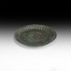 Islamic Silver-Inlaid Plate
13th-14th century AD. A shallow bronze dish with raised rim and fluted detailing, silver-inlaid pellets to the rim, dense...