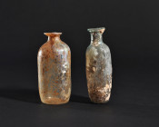 ARQUEOLOGÍA. ROMA. Lote de 2 ungüentarios cilíndricos (ss. I-IV d.C.). Vidrio con irisaciones. Altura de 9,5 a 10,4 cm. Uno de ellos presenta una grie...