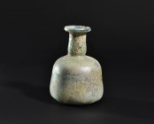 ARQUEOLOGÍA. ROMA. Ungüentario de cuerpo troncocónico, cuello cilíndrico y boca exvasada (ss. I-IV d.C.). Vidrio con irisaciones. Altura 12 cm.