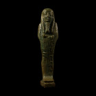 Late Period, circa 4th century B.C. Of mummiform type, wearing a tripartite wig and long plaited divine beard; holding a pick in the left hand, a hoe ...