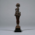 Late Period, 664-332 B.C. Modelled in the round figure of Khonsu standing, holding the crook, flail, and long was-sceptre, with false beard and sidelo...