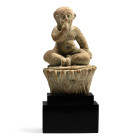 Late Period, circa 664-332 B.C. Modelled in the round, the nude seated figure of the child Somtous, with one hand to his lips and a prominent sidelock...