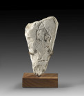 Limestone fragment broken all around except the front, H 15cm, W 7.5cm, D 5cm. The relief depicts the head of Akhenaten, wearing a Nubian wig, in deep...