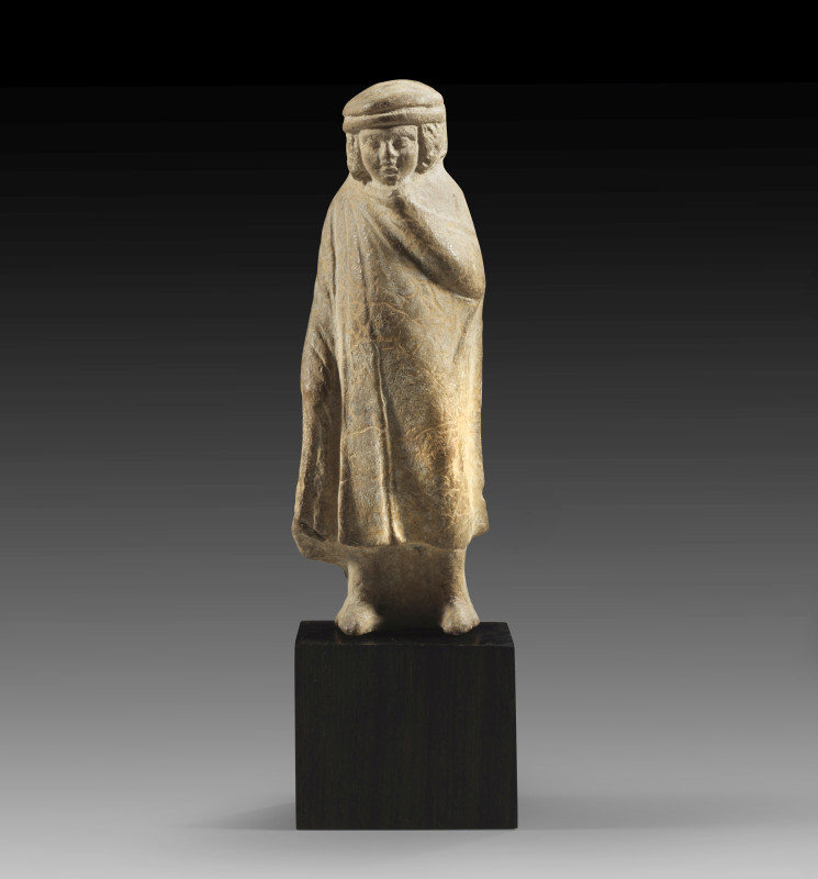 A greek hellenistic terracotta figure of a young pilgrim wearing a long cloak an...