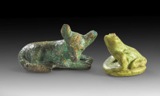 Two animal amulets: a) L 2.2cm. Made of steatite with green faience glaze. Reclining dog. Wax residue on the underside. With plexiglass base. Late Per...