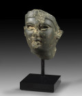 Ptolemaic portrait, 3rd - 1st century BC. Dark grey, greenish stone. Head with almond shaped eyes, fleshy cheeks, a small nose and mouth and a knobby ...