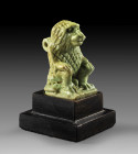 Amulet of Thot: H 3.5cm. Light green faience. A baboon crouching on a plinth, its tail wrapped around its body, its front paws resting on its bent hin...