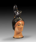Attic head oinochoe of the Cook Class. 480 - 460 BC. H with handle 17.4cm, W of the head 6.5cm. Jug with treefoil mouth and high stirrup handle in the...