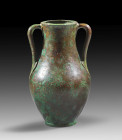 Thick-walled, heavy bronze amphora with ovoid corpus and slightly swinging neck. Turned base with concentric, profiled circles. Handles with lancet-sh...