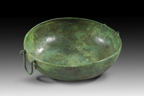 Bronze bowl with a flat bottom and curved walls with an inward-sloping lip. Concentric incised circles in the center. Two omega-shaped handles. Roman ...