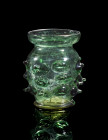 Krautstrunk. ø 8cm; H 9cm. Germany, 15th century AD. Blue green glass. Barrel-shaped body with nubs on a standing ring. Broad lip over the constricted...