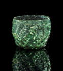 Maigelein. ø 8cm; H 6,5cm. Germany, 15th century AD. Blue green glass. High rim decorated with a basket pattern. The base is very high. Crack in rim. ...