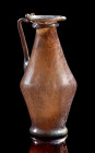 Auberginefarbenes Kännchen. Römisch, 3. - 4. Jh. n. Chr. H 16cm. Schlanker, bikonischer Corpus aus auberginefarbenem Klarglas mit Standplatte und weit...