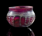 Hohe Rippenschale. Römisch, ca. 1. Jh. n. Chr. ø 8cm; H 5,8cm. Auberginefarbenes Glas mit weißer Fadenauflage. Hohe Wandung. Außen schmale, sich zum Z...