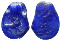 This is a small, oval-shaped ancient gem or seal made from a translucent deep blue material, likely glass or a semi-precious stone such as lapis lazul...