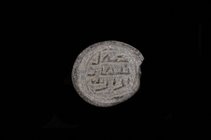 An Islamic Glass Seal, uniface, in grey-green glass, with three-line inscription in angular Kufic, possibly to be read as ‘amil | Luqman | ibn Yazid, ...